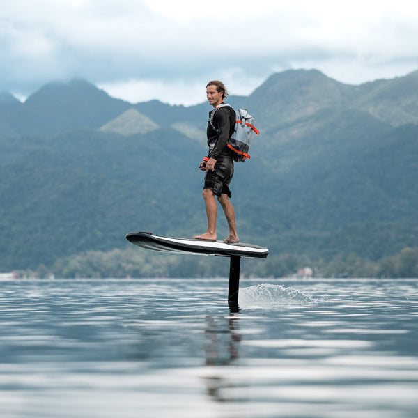 A man is soaring above the water on an Awake VINGA 3 efoil against a backdrop of lush green mountains in Thailand.