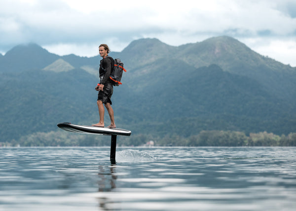 A man is soaring above the water on an Awake VINGA 3 efoil against a backdrop of lush green mountains in Thailand.