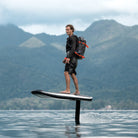 A man is soaring above the water on an Awake VINGA 3 efoil against a backdrop of lush green mountains in Thailand.